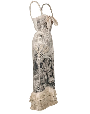 The Invictus Ankle Dress by Johanna Ortiz is a sleeveless linen dress featuring a botanical print, ribbon detail at the bust, braided straps, and a layered fringe hem for an elegant, breezy look.