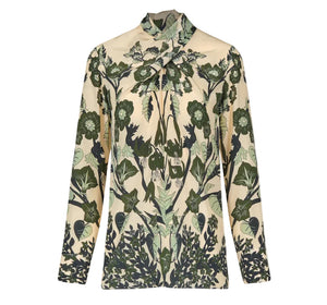 The Heavenly Garden Top by Johanna Ortiz is a long-sleeved cream silk CDC blouse with a high neck, adorned with the brand’s signature green botanical leaf and flower motif.