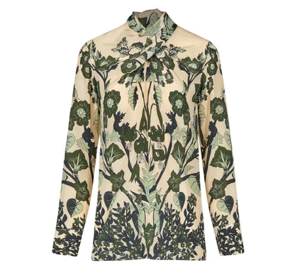 The Heavenly Garden Top by Johanna Ortiz is a long-sleeved cream silk CDC blouse with a high neck, adorned with the brand’s signature green botanical leaf and flower motif.