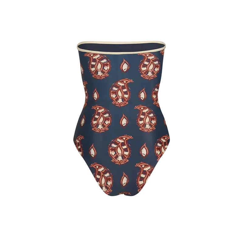 The Alta Mar One Piece by Johanna Ortiz is a strapless swimsuit featuring a navy background with red and white paisley patterns, elegantly displayed on a white backdrop.