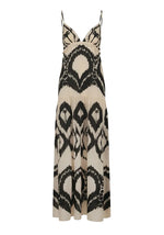 The Zea Palm Maxi Dress by Johanna Ortiz is a sleeveless, cream-colored dress featuring an empire waist, thin adjustable straps, and a striking black abstract pattern.