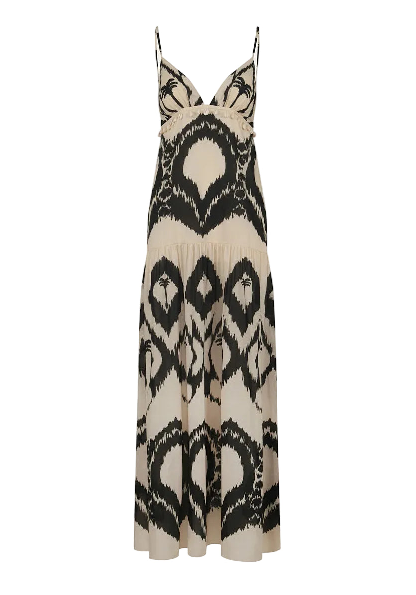 The Zea Palm Maxi Dress by Johanna Ortiz is a sleeveless, cream-colored dress featuring an empire waist, thin adjustable straps, and a striking black abstract pattern.