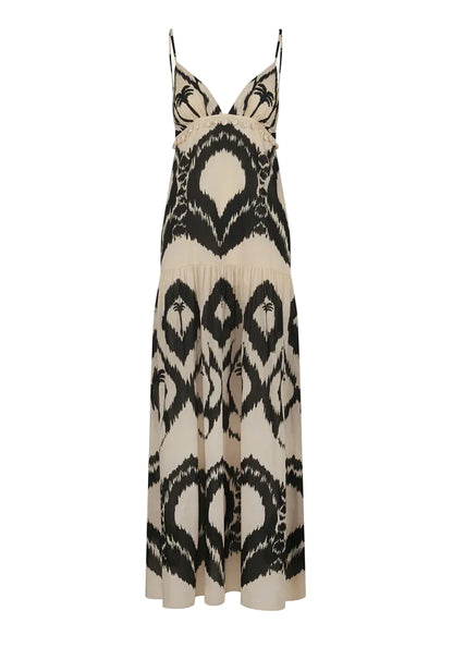 The Zea Palm Maxi Dress by Johanna Ortiz is a sleeveless, cream-colored dress featuring an empire waist, thin adjustable straps, and a striking black abstract pattern.