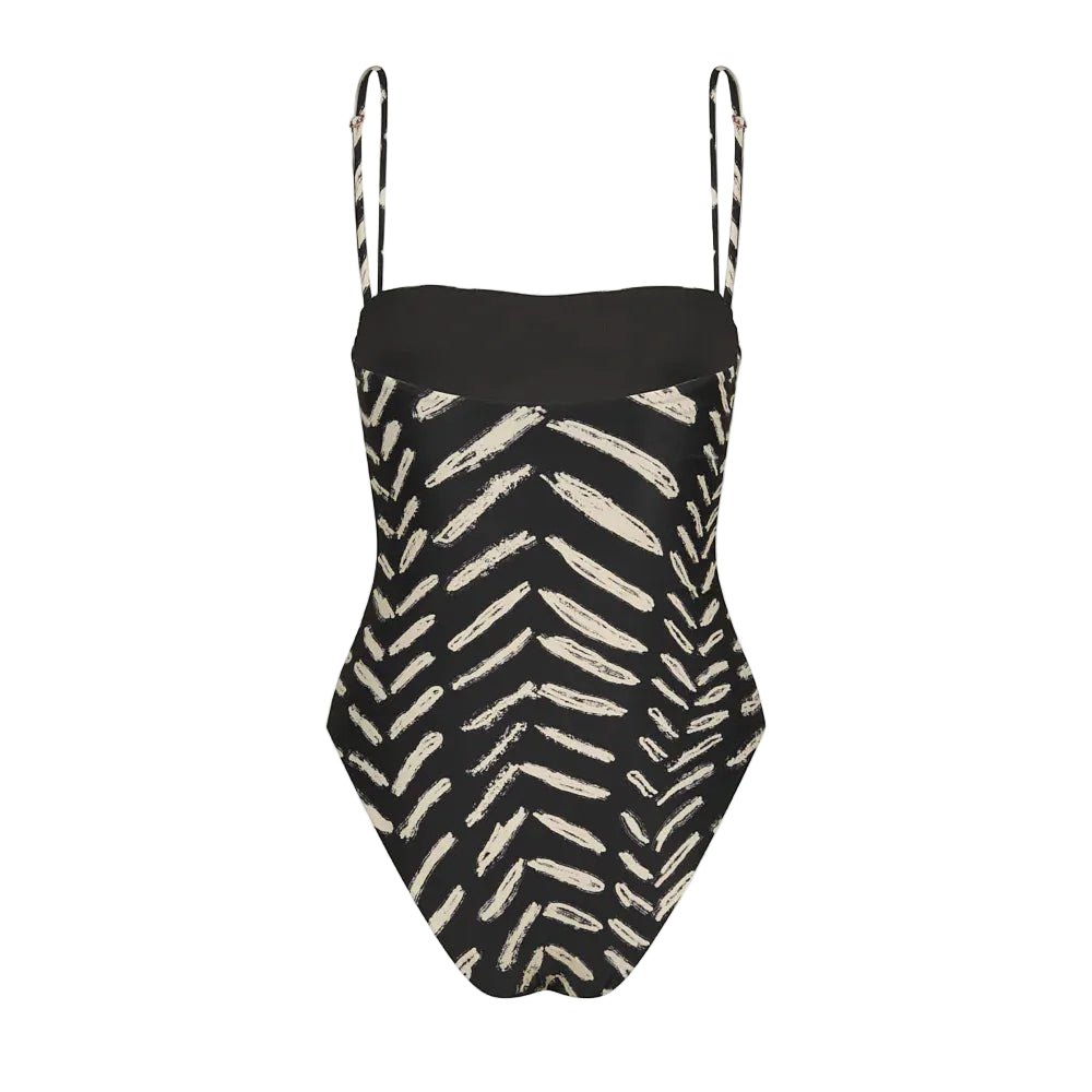 The Whispering Tides One Piece by Johanna Ortiz is a black swimsuit with thin straps and a bold white JO print reminiscent of leaves or chevrons.