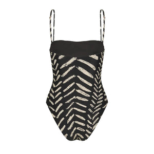 The Whispering Tides One Piece by Johanna Ortiz is a black swimsuit with thin straps and a bold white JO print reminiscent of leaves or chevrons.