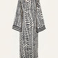 The Squared Away Tunic Dress by Johanna Ortiz is a long robe-style dress featuring a black and white herringbone pattern, wide sleeves, and black trim at the cuffs and hem. Structured shoulders create a tailored silhouette, as shown from the back against a plain background.