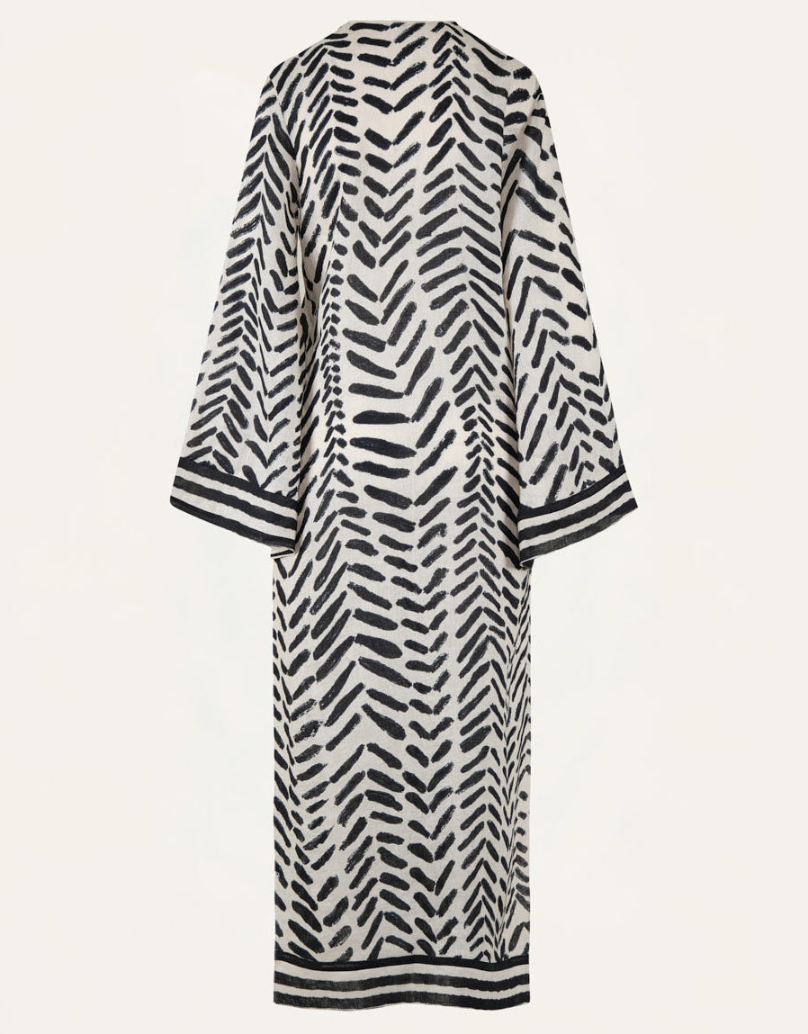 The Squared Away Tunic Dress by Johanna Ortiz is a long robe-style dress featuring a black and white herringbone pattern, wide sleeves, and black trim at the cuffs and hem. Structured shoulders create a tailored silhouette, as shown from the back against a plain background.
