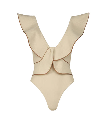 The Crinkle Beaches One Piece by Johanna Ortiz is a cream-colored crinkle lycra swimsuit with wide ruffled straps, brown edging, and a large decorative bow on the back—an elegant choice for the beach.