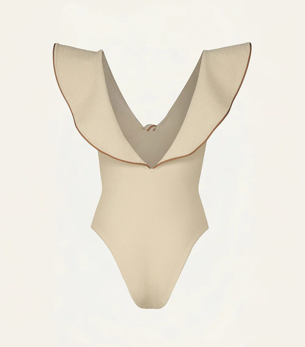 The Crinkle Beaches One Piece by Johanna Ortiz is a beige swimsuit made from crinkle lycra, showcasing a deep V-neck and wide ruffled shoulders for a chic beach look.