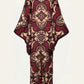 One Palm Only Tunic Dress by Johanna Ortiz featuring long sleeves and a floor-length silhouette, adorned with a maroon and beige baroque floral pattern and subtle Equine Mola motif accents, shown from the back against a plain light background.
