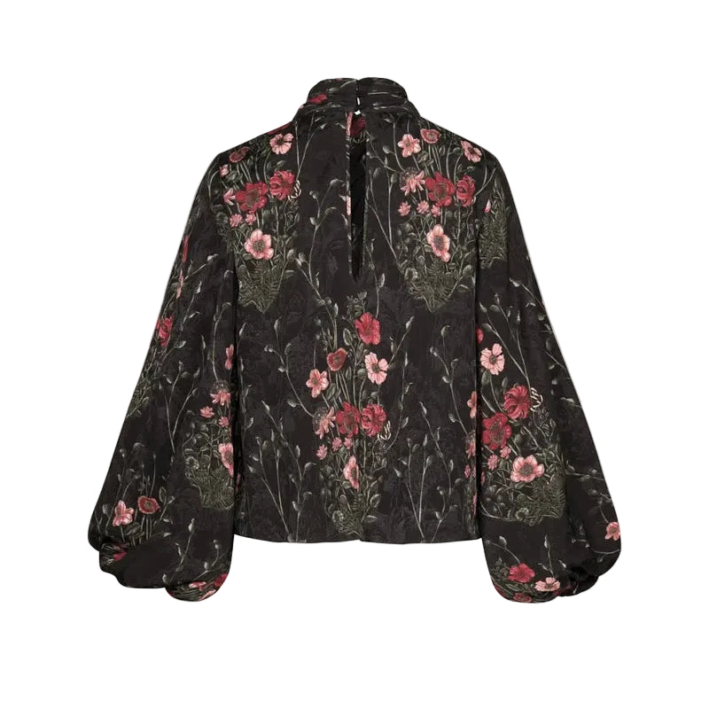 Back view of the Johanna Ortiz Jacquard Intricate Islands Top, a long-sleeved black blouse with a red and pink botanical motif, a high neckline, and a keyhole opening.