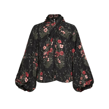 Johanna Ortiz Jacquard Intricate Islands Top in black, featuring a high neck, long sleeves, knotted front detail, and a red and pink botanical floral jacquard pattern.