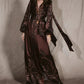 Johanna Ortiz Timeless Concurse Wrap Dress in dark brown silk, featuring a wrap design, long sleeves, neck tie, and light-colored botanical motifs on the hem and sleeves.