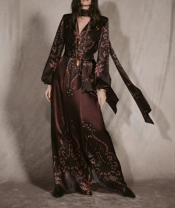 Johanna Ortiz Timeless Concurse Wrap Dress in dark brown silk, featuring a wrap design, long sleeves, neck tie, and light-colored botanical motifs on the hem and sleeves.