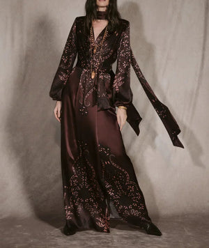 Johanna Ortiz Timeless Concurse Wrap Dress in dark brown silk, featuring a wrap design, long sleeves, neck tie, and light-colored botanical motifs on the hem and sleeves.