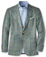 A Peter Millar Tremont Plaid Soft Jacket in green and blue plaid Italian wool, worn over a light blue dress shirt, featuring two front pockets and complemented by a white pocket square.