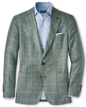 A Peter Millar Tremont Plaid Soft Jacket in green and blue plaid Italian wool, worn over a light blue dress shirt, featuring two front pockets and complemented by a white pocket square.