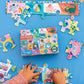 A child assembles Eeboo’s Learn the Alphabet 20 Piece Puzzle with vibrant animal illustrations and letters on a blue surface; completed sections and the puzzle box are also shown.