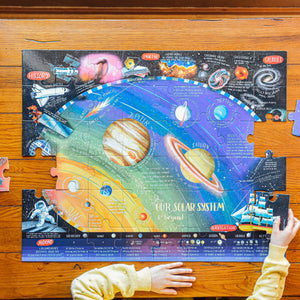 A child assembles the Eeboo Solar System and Beyond 48-Piece Giant Puzzle on a wooden table, enjoying an educational jigsaw filled with planets, interesting facts, and vivid illustrations that inspire curiosity about space.