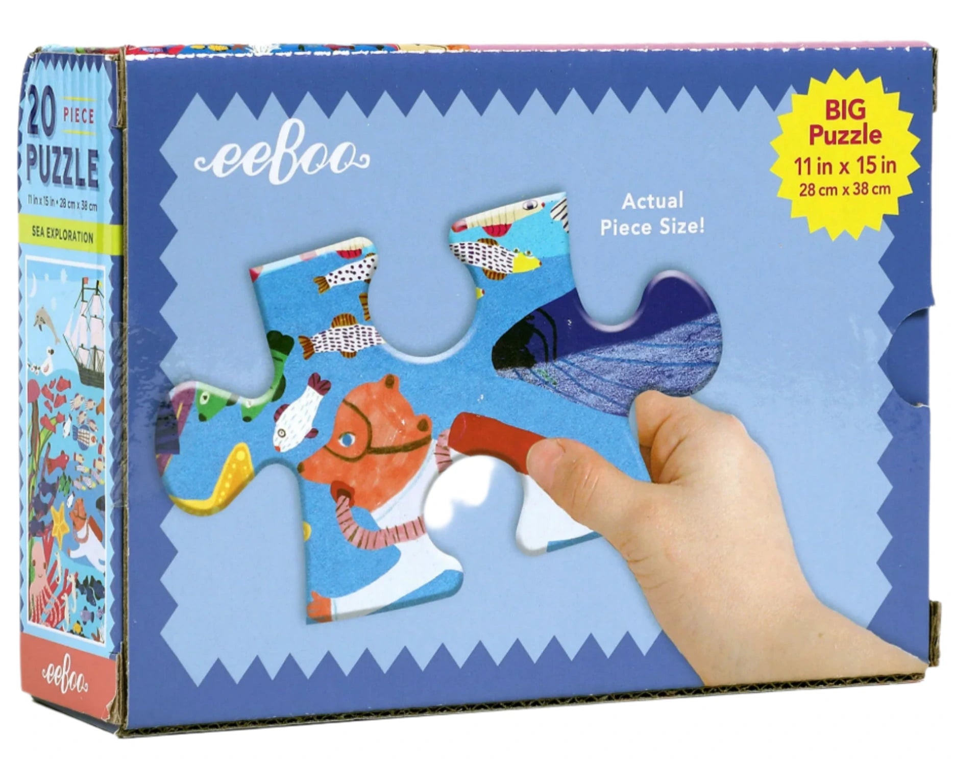 A hand holds a large puzzle piece in front of the Eeboo Sea Exploration 20 Piece Big Puzzle box, featuring vibrant artwork and showcasing its big 11"x15" size.