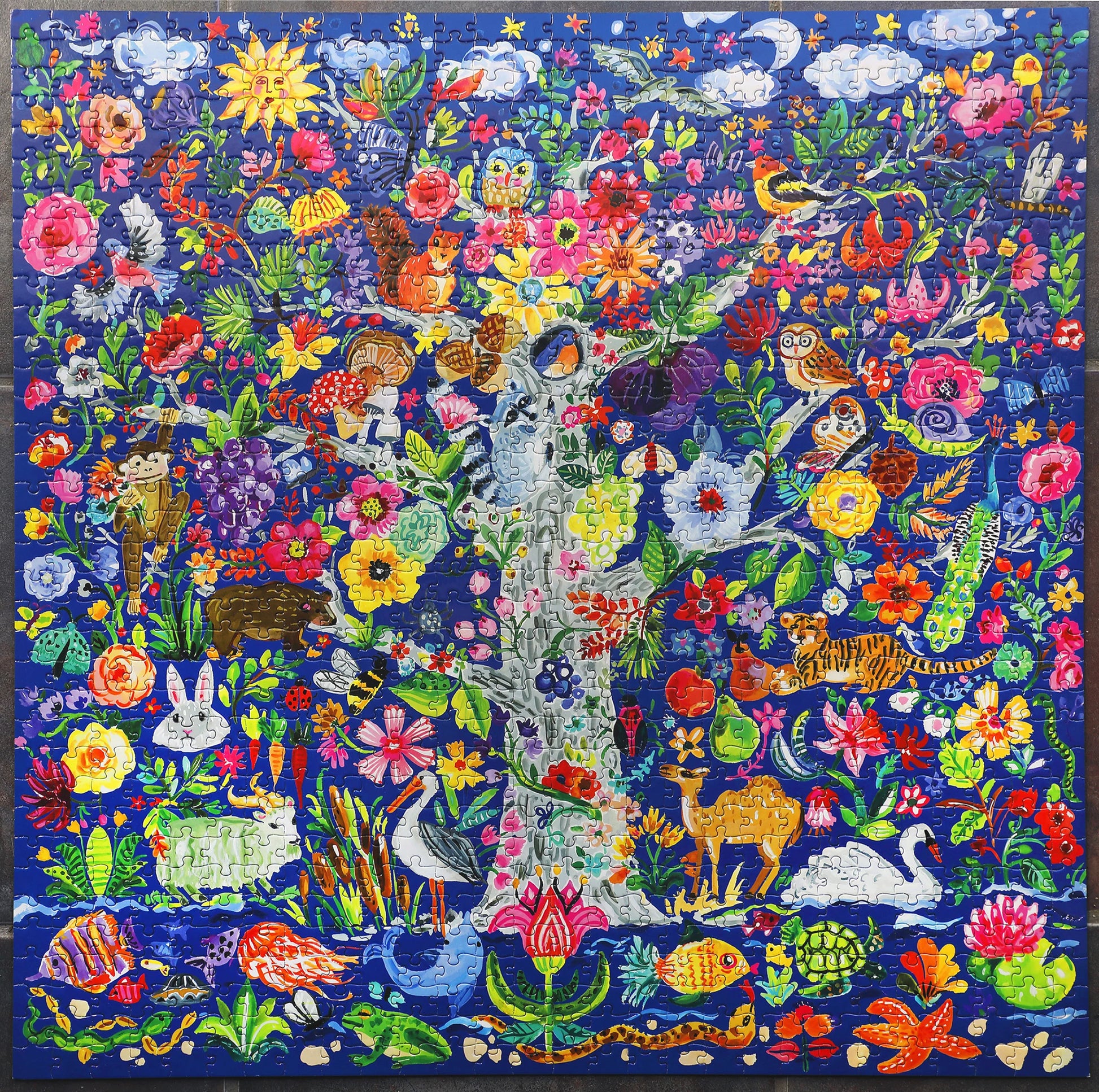 Bring home the Eeboo Tree of Life Puzzle—a vivid 1000 piece jigsaw puzzle featuring a colorful illustration of a tree filled with diverse animals and vibrant flowers against a blue background. Discover creatures like tigers, swans, owls, rabbits, and fish nestled in lush foliage—perfect for your next family activity.