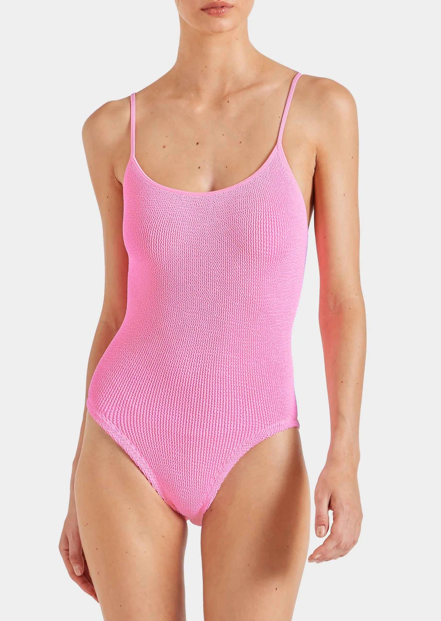 Wearing Hunza G's Pamela Swim, a textured, bright pink one-piece in Original Crinkle fabric with thin straps—shown from shoulders to upper thighs—offers adjustable coverage and the comfort of one size swimwear.