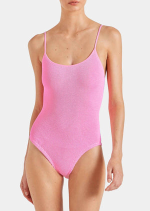 Wearing Hunza G's Pamela Swim, a textured, bright pink one-piece in Original Crinkle fabric with thin straps—shown from shoulders to upper thighs—offers adjustable coverage and the comfort of one size swimwear.