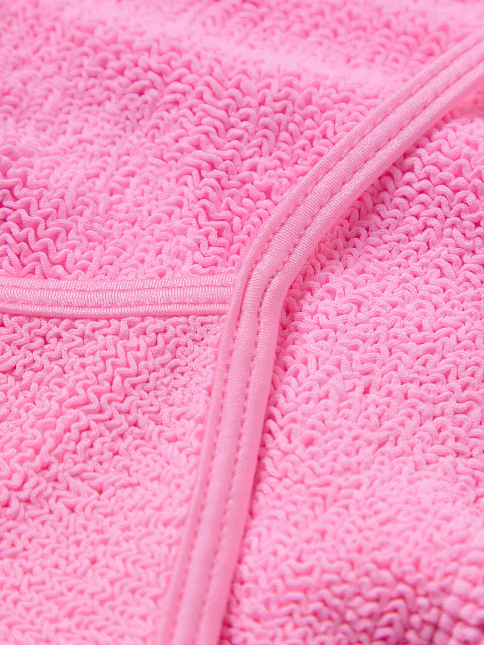 Close-up of Hunza G’s Pamela Swim in pink, showcasing the textured Original Crinkle fabric and a diagonal seam with visible stitching.