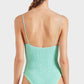 A woman with long brown hair in a braid is shown from the back against a plain white background, wearing the Pamela Swim by Hunza G—a textured light green one-piece swimsuit crafted from Original Crinkle™ fabrication with thin straps.