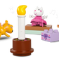Three LEGO® Peppa Pig DUPLO figures, a toy dog, and a cake with candle gather by colorful bricks from the LEGO® Peppa Pig Birthday House set, capturing a joyful Peppa Pig birthday celebration.