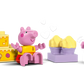 Two pink pig figures face each other with yellow LEGO® DUPLO® blocks and a purple tray between them in the LEGO® Peppa Pig Boat Trip set, making it a perfect preschool learning toy. White hearts are illustrated above the tray.