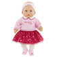 Introducing the Corolle Albane Heart Petals Doll, crafted by Corolle. This delightful baby doll features soft vinyl skin and is dressed in a charming pink headband, a pink top, a red skirt embellished with hearts, white tights, and adorable pink shoes. She stands elegantly against a plain white background.