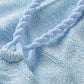 A close-up of the Phoebe Bikini by Hunza G in light blue crinkle fabric, featuring a braided strap, is shown lying on top.