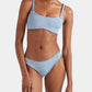 A person wears the Hunza G Phoebe Bikini, featuring textured light blue crinkle fabric and twisted shoulder straps, standing against a plain white background.