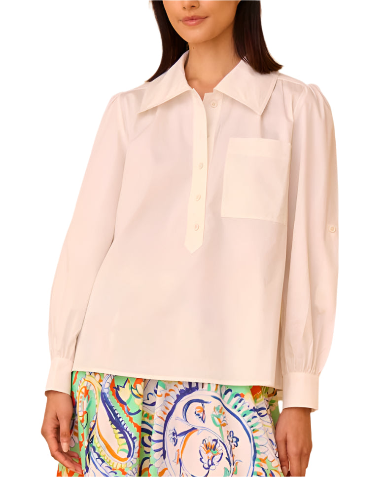 A person wearing the Hunter Bell Phoenix Shirt by Hunter Bell NYC, featuring a tailored collared neckline and a pocket, paired with a patterned skirt showcasing colorful designs.