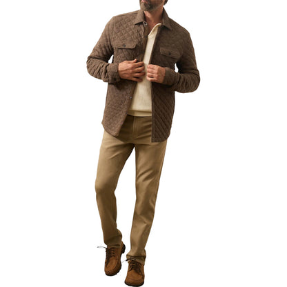 A man wears the Faherty Epic Quilted Fleece jacket over a cream shirt, tan pants, and brown shoes, standing against a white background.