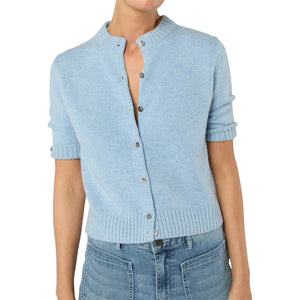 A person wearing the Ann Mashburn Kelly Cardigan—a light blue, short-sleeve Mongolian cashmere button-up with top buttons undone—paired with high-waisted blue jeans for a stylish, versatile look.