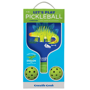 The Crocodile Creek Dinosaur Pickleball Set for kids ages 6+ includes a junior fiberglass paddle with a dinosaur design, two green pickleballs, and comes in vibrant blue and white packaging.