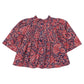 The Pink Chicken Girls’ Jaipur Top is a long-sleeved baby shirt showcasing a red and white paisley pattern on a dark blue background, accented with navy glitter buttons at the front and a gathered waist.