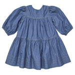 A Girls’ Sawyer Dress by Pink Chicken in blue, knee-length with long puff sleeves, showcases gathered tiers and stitching details near the hem, displayed flat on a white background.
