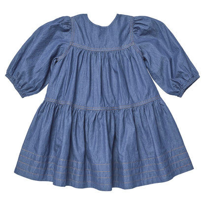 A Girls’ Sawyer Dress by Pink Chicken in blue, knee-length with long puff sleeves, showcases gathered tiers and stitching details near the hem, displayed flat on a white background.