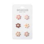 A white card labeled “Kids’ Bike Basket Pins” by Banwood displays six daisy-shaped pins in pink, brown, and beige tones, arranged in two columns and three rows—the perfect collectible accessory for your Pin & Ride Baskets.
