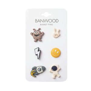 A card labeled “Banwood Kids’ Bike Basket Pins” displays six collectible pins—featuring a monster, peace sign, lightning bolt, smiley face, rocket, and astronaut—perfect for decorating your Pin & Ride Baskets with playful Banwood style.