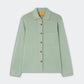 The Pinstripe Work Shirt by Guest in Residence is a light green, long-sleeve button-down crafted from a cotton-silk blend. It features thin vertical beige pinstripes, a single chest pocket, and a pointed collar. The shirt is presented against a plain light gray background.