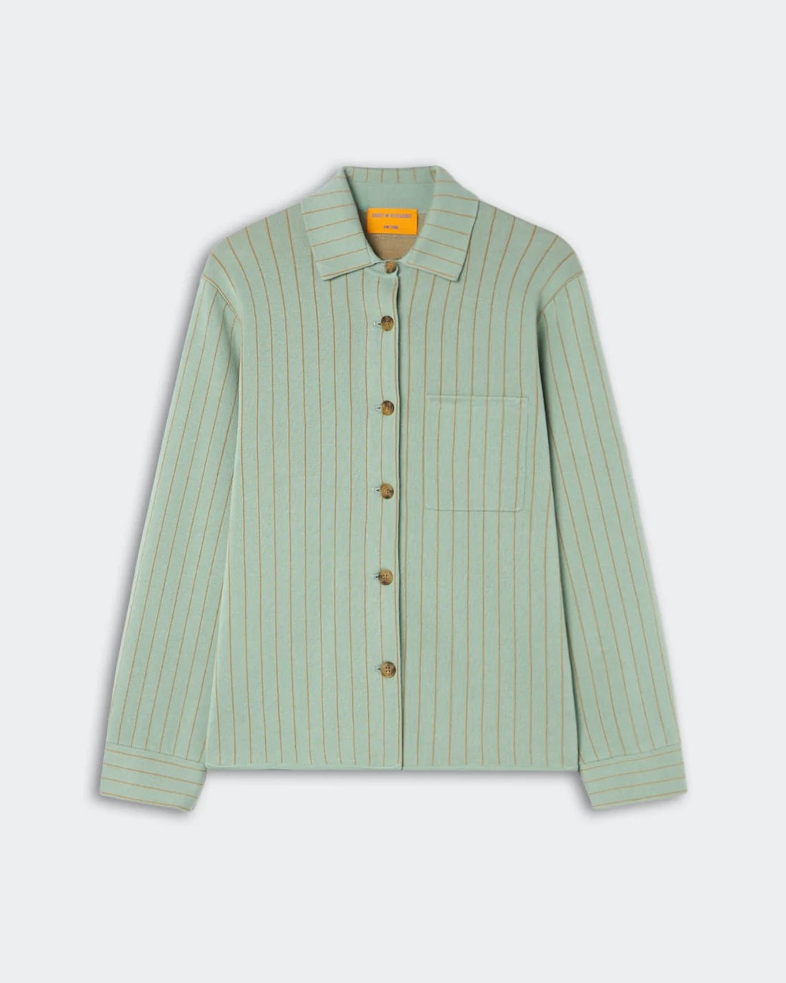 The Pinstripe Work Shirt by Guest in Residence is a light green, long-sleeve button-down crafted from a cotton-silk blend. It features thin vertical beige pinstripes, a single chest pocket, and a pointed collar. The shirt is presented against a plain light gray background.