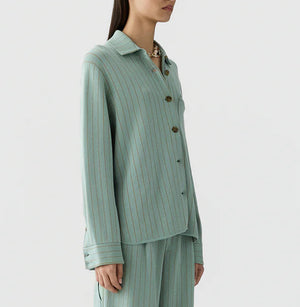 A woman wearing the Guest in Residence Pinstripe Work Shirt in light green with vertical stripes and matching loose-fitting pants, standing against a plain background.
