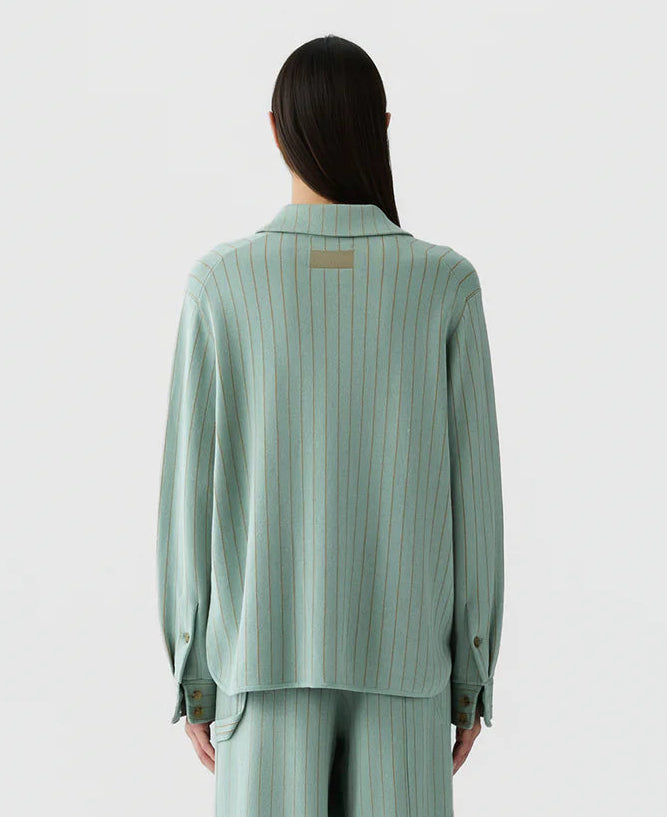 A person with long dark hair is shown from the back against a plain light background, wearing the Guest in Residence Pinstripe Work Shirt and matching pants. The loose fit and subtle vertical stripes of the cotton-silk button-down ensemble create an effortlessly elegant look.