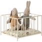 Two Maileg stuffed rabbits in knitwear sit inside a Maileg Playpen, Micro, placed on a patterned cushion.