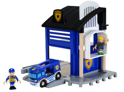 The BRIO World Police Station by Brio includes a garage, a blue police truck, and two toy figures—one dressed in a uniform and the other in casual attire. It also features a secure prison cell for imaginative play.