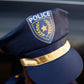 Someone wearing a navy blue police hat with gold band and badge from the Great Pretenders Police Officer Set; their face is mostly hidden, making it ideal for dress-up or imaginative play.